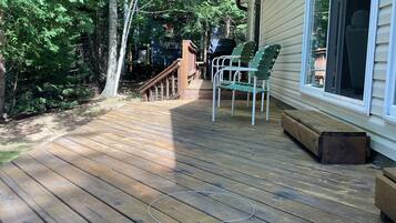 Een houten terras met twee groene stoelen, een barbecue en een houten bank.