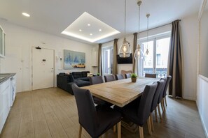 A modern living room with a wooden dining table, black sofas, and a large window with curtains.