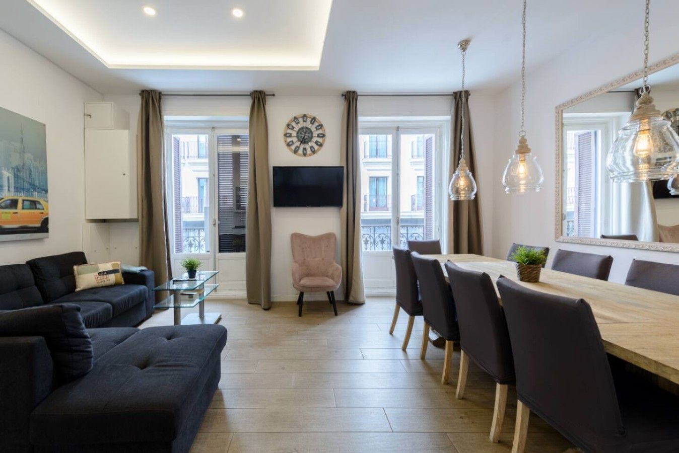 Una sala de estar moderna con un sofá, una mesa de comedor con sillas, un televisor montado en la pared y un espejo grande.