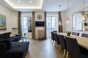 A modern living room with a sofa, a dining table with chairs, a TV mounted on the wall, and a large mirror. - 4br 2bth best location SOl, new (Madrid)