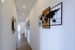 A hallway with a wooden floor, white walls, and artwork including a world map. - 4br 2bth best location SOl, new (Madrid)