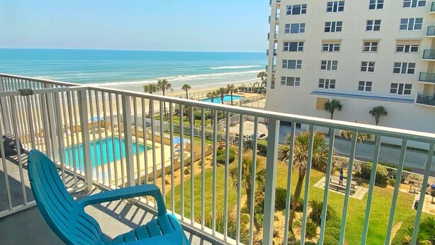 Un balcon avec des chaises turquoise donnant sur une piscine et une plage.