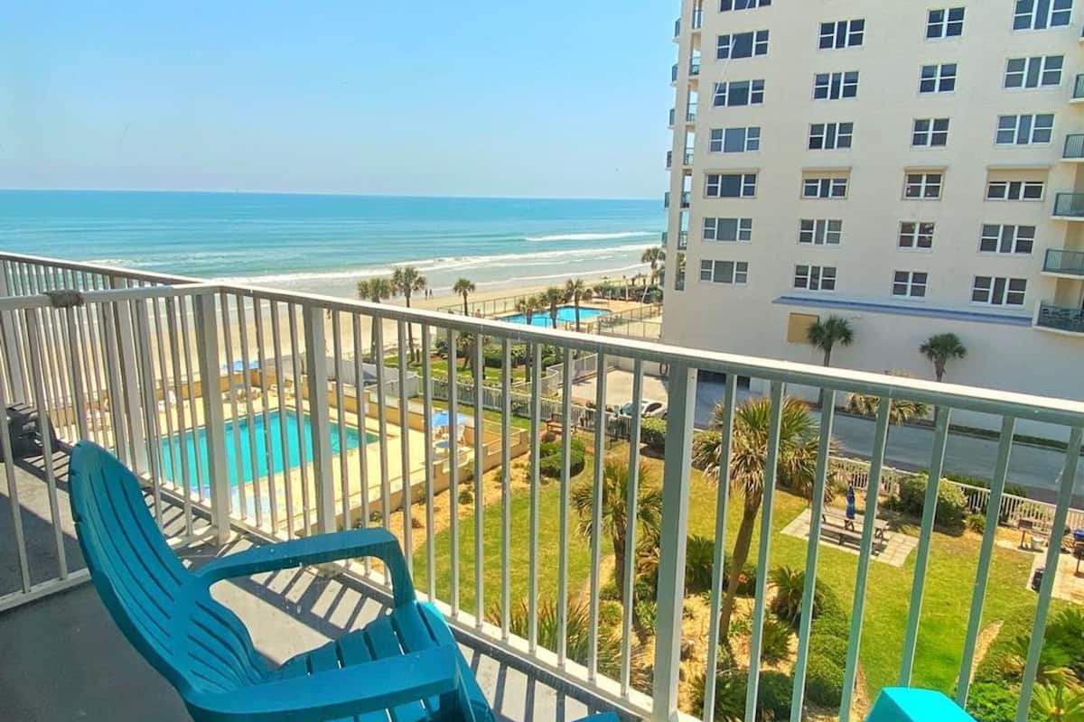 Een balkon met turquoise stoelen met uitzicht op een zwembad en een strand.
