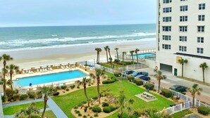 Un hôtel doté d’une piscine, offrant une vue sur la plage et bordé de palmiers.