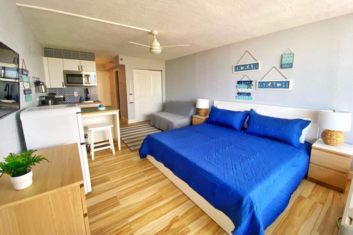 Een compacte slaapkamer met een bed, nachtkastjes, een bureau en een kitchenette.