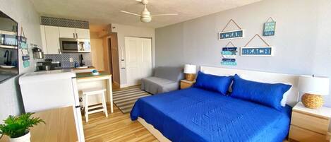 A compact bedroom with a bed, bedside tables, a desk, and a kitchenette.