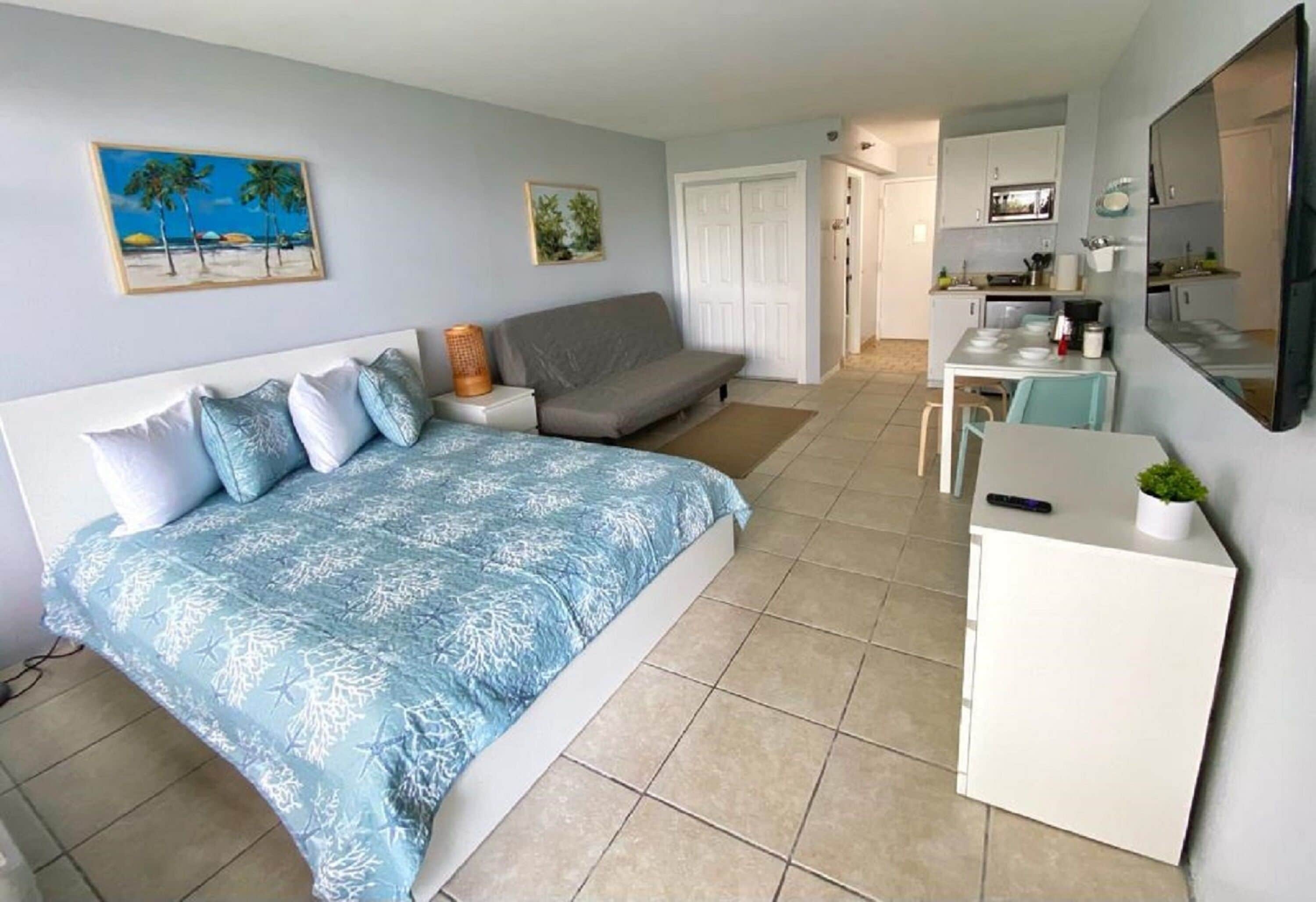 A bedroom with a bed, a sofa, a desk, and a kitchenette.