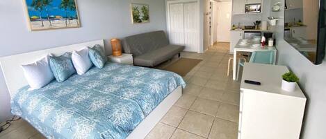 A bedroom with a bed, a sofa, a desk, and a kitchenette.
