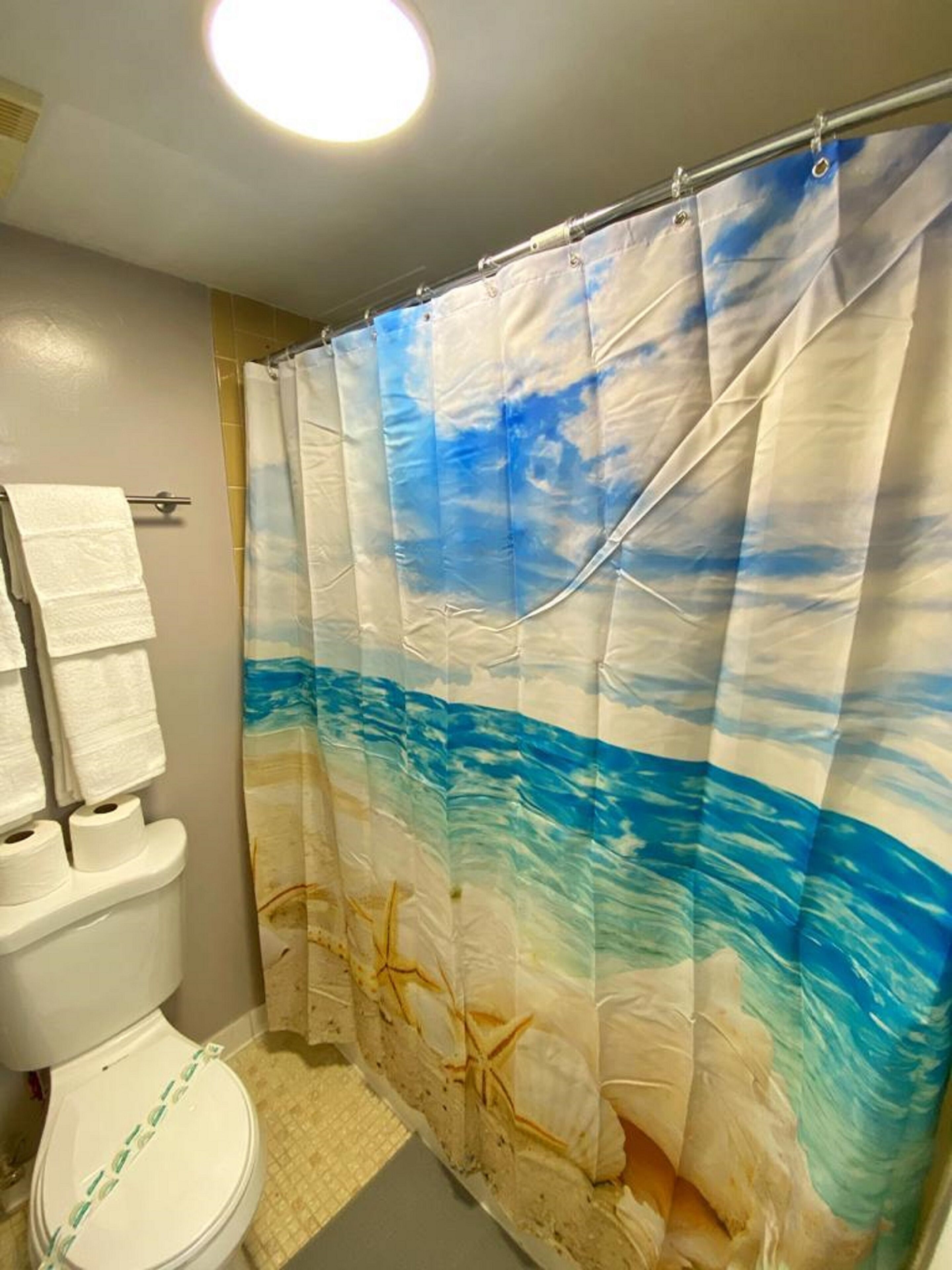 Un baño con inodoro, toallero y cortina de ducha con diseño de playa.