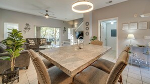 A spacious living room with a large dining table, comfortable seating, and a ceiling fan.
