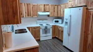 A kitchen with wooden cabinets, a white stove, a microwave, and a refrigerator. - Raven's Roost - Beaver Lake (Kodiak)