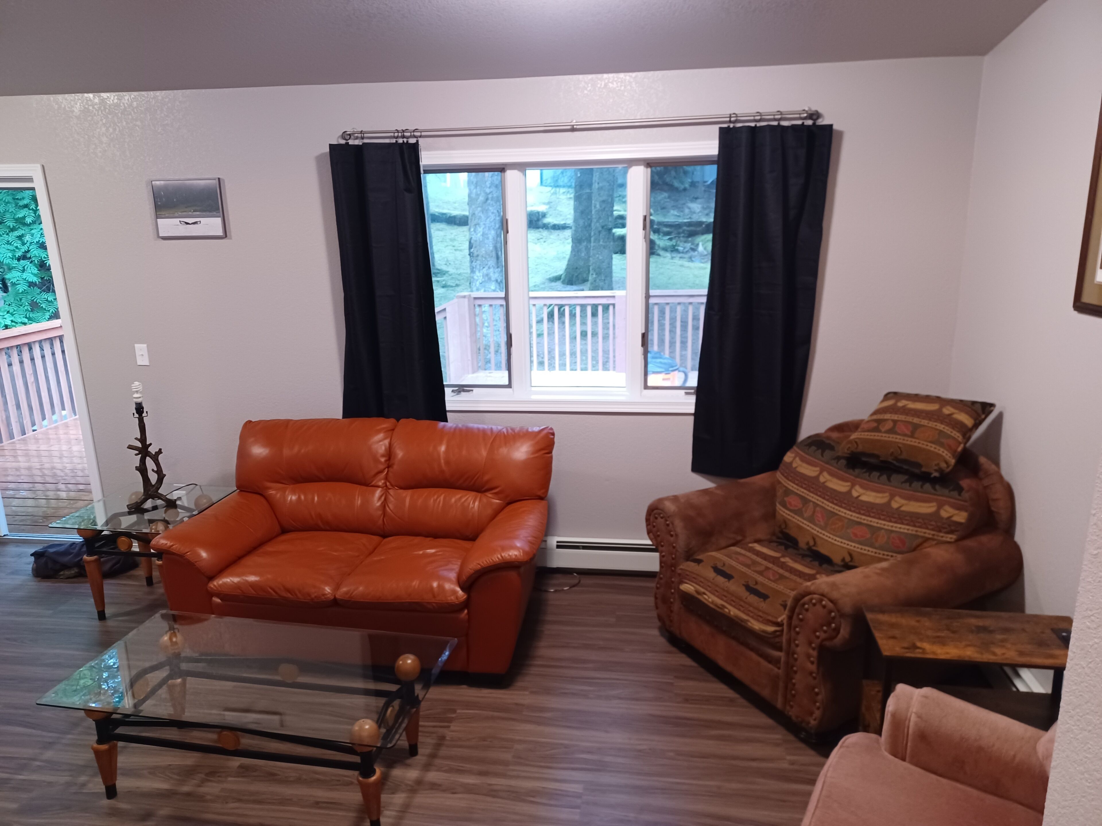 A living room with a brown leather sofa, a glass coffee table, and a patterned armchair.