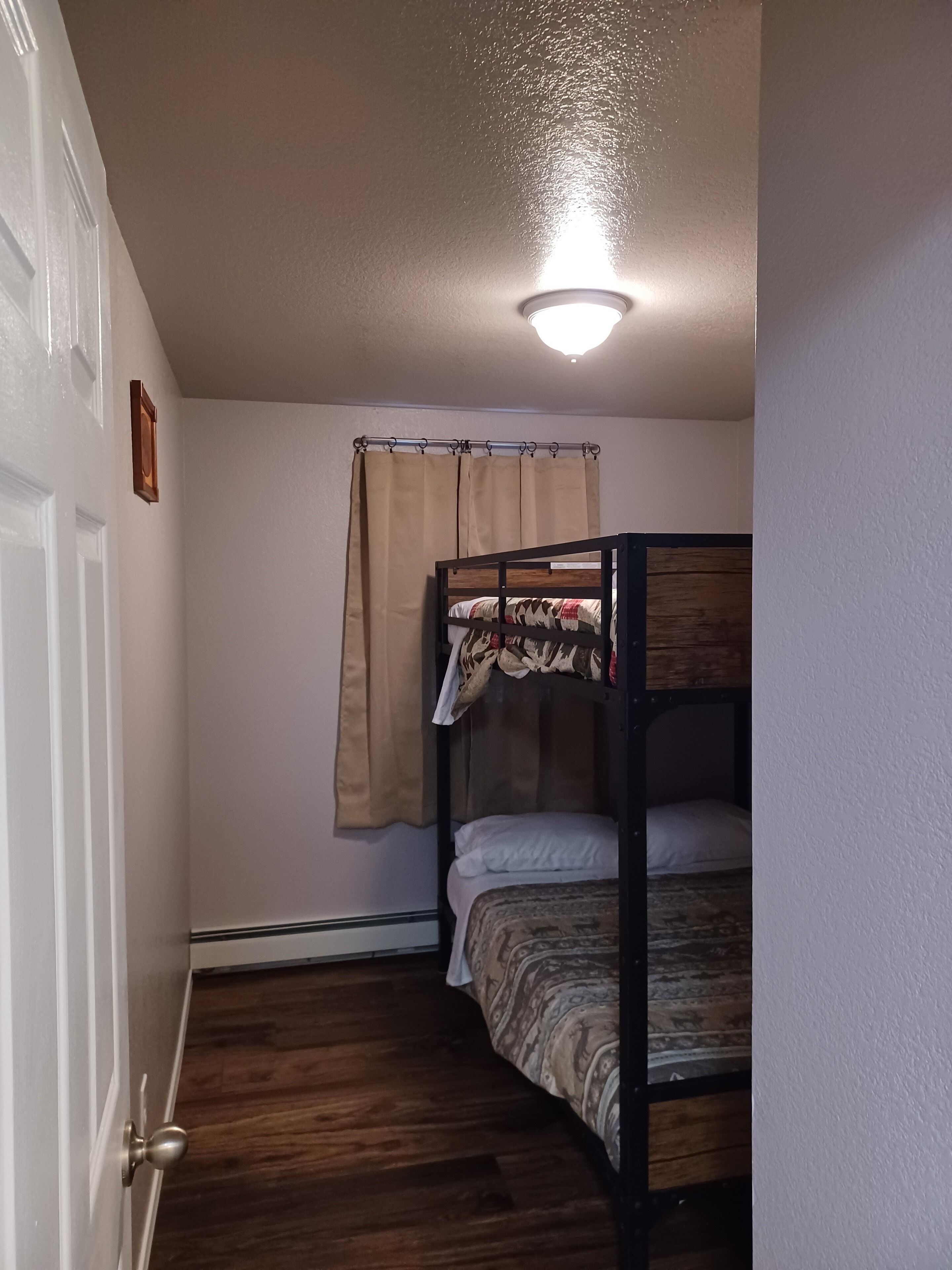 Una habitación con literas, una puerta, una lámpara y una cortina.