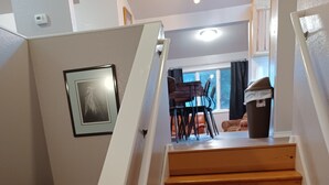 A wooden staircase with white handrails leading to a dining area with chairs and a table. - Raven's Roost - Beaver Lake (Kodiak)