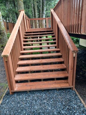 Stairs lead up to a deck surrounded by lush greenery and trees.