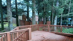A wooden deck with railings, surrounded by tall trees and a wooden fence. - Raven's Roost - Beaver Lake (Kodiak)