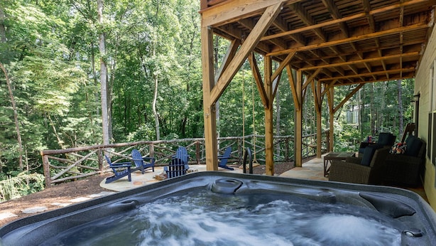 Un jacuzzi con cubierta de madera y sillas, rodeado por un bosque.