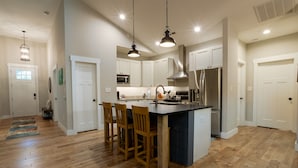 Una cocina moderna con una isla central, sillas de madera, electrodomésticos de acero inoxidable e iluminación colgante.
