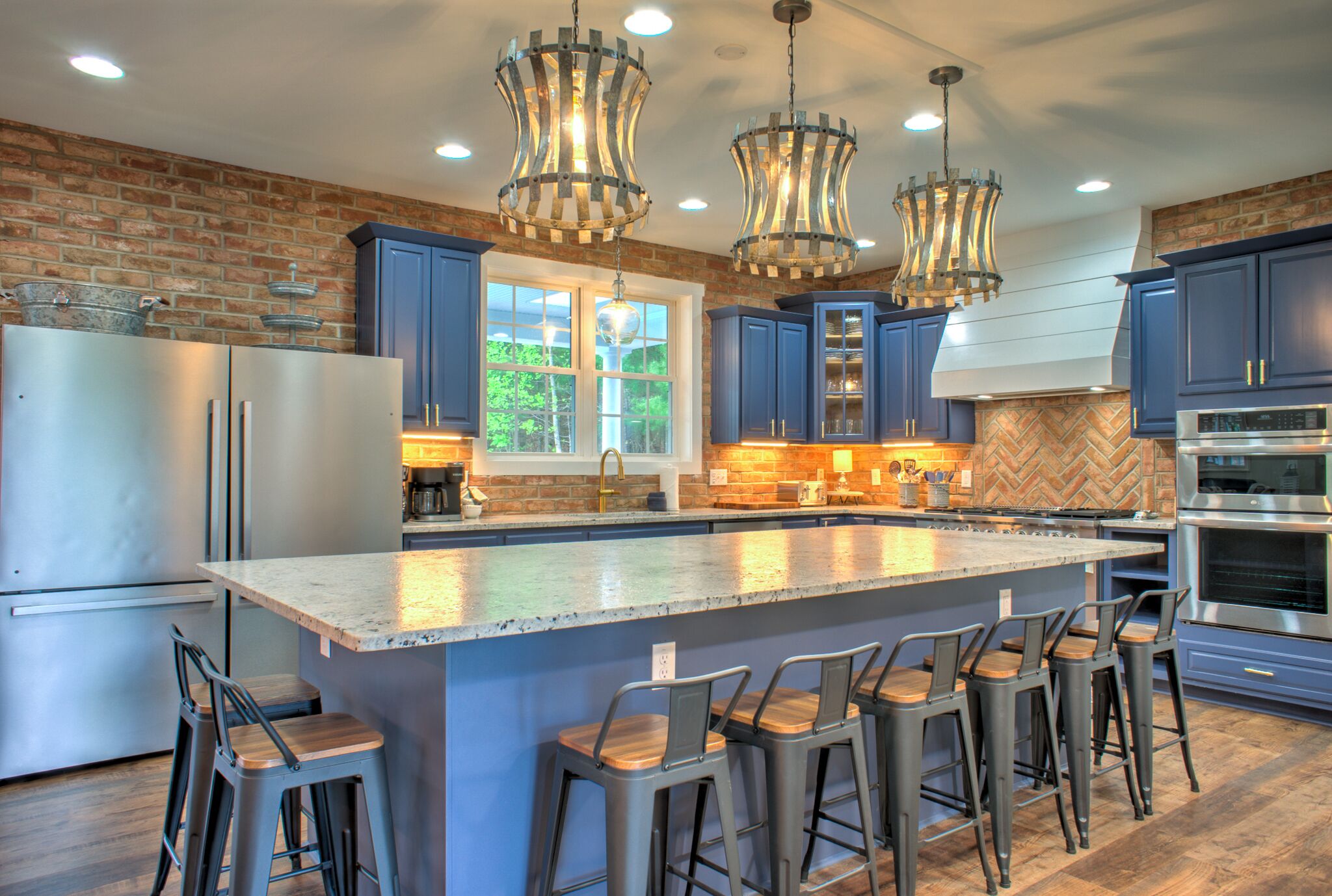 A modern kitchen with blue cabinets, a large island with bar stools, stainless steel appliances, and unique pendant lighting.