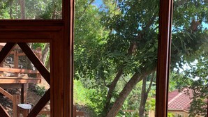Une terrasse en bois avec une balustrade blanche, entourée d’arbres et, au fond, d’un bâtiment au toit rouge.