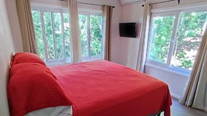 Une chambre à coucher avec un lit, un ventilateur de plafond, une télévision et de grandes fenêtres.