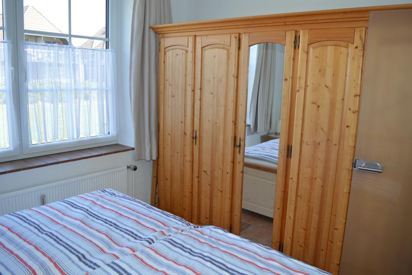 A bedroom with a bed, wooden wardrobe, and a window with curtains.
