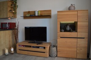 Un salon moderne doté d’un téléviseur à écran plat, de meubles en bois et d’étagères où sont disposés des livres et des objets décoratifs.