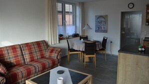 A living room with a plaid sofa, a dining table with chairs, a small table with a candle, and a window with curtains. - Ferienwohnung Wohnpark Warfstr. 5/4 - Wohnpark Werdum (Werdum)