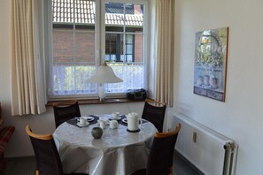 Comedor con mesa lista para cuatro personas, lámpara y ventana con cortinas.