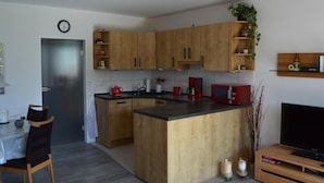 A modern kitchen with wooden cabinets, a microwave, a coffee maker, and a dining area with a table and chairs. - Ferienwohnung Wohnpark Warfstr. 5/4 - Wohnpark Werdum (Werdum)