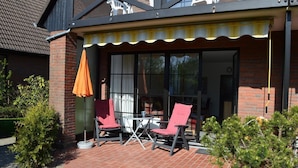 A patio with two red chairs and a table, a brick wall, and a yellow awning. - Ferienwohnung Wohnpark Warfstr. 5/4 - Wohnpark Werdum (Werdum)