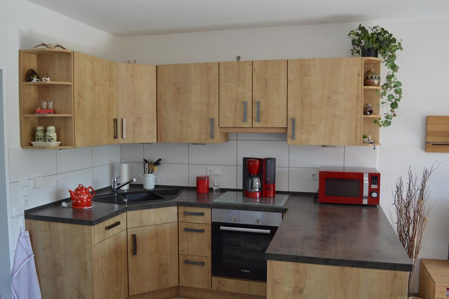 Une cuisine moderne avec des meubles en bois, un lave-vaisselle Bosch, un micro-ondes rouge et une machine à café.