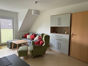 Un salon moderne avec un canapé gris, des fauteuils verts, une table basse en bois et un meuble gris avec des tiroirs.
