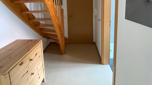 A narrow hallway with a wooden staircase on the left, a door at the end, and a wall-mounted light fixture. - Ferienwohnung Am Harlebogen 10 Whg. 4 (Wittmund)