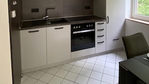 A compact kitchen with white cabinets, a black countertop, and a built-in oven. - Ferienwohnung Am Harlebogen 10 Whg. 4 (Wittmund)