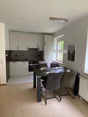 Une cuisine moderne avec des meubles blancs, un plan de travail noir et un coin repas comprenant une table et des chaises.