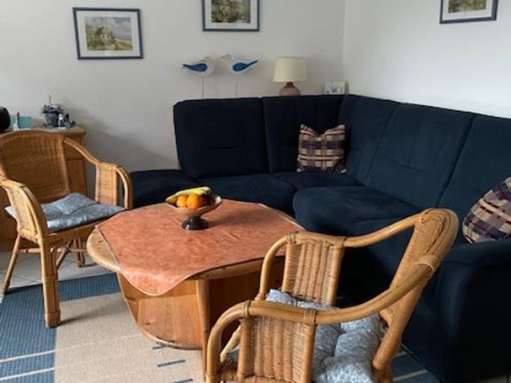 A living room with a dark blue sofa, two wicker chairs, a small round table with a fruit bowl, and a lamp.
