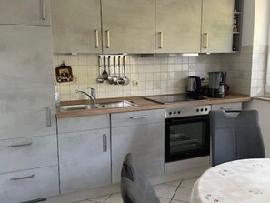 Une cuisine avec des meubles gris, un four en acier inoxydable, une machine à café et un évier.
