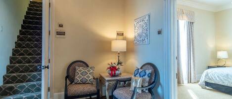 A hotel room with a staircase, two chairs, a small table with a lamp, and a bed.