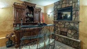 A bar area with a stone fireplace, a wooden bar counter, and a decorative cabinet with bottles. - Penthouse King Suite•Private Floor•Monterey (Salinas)