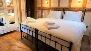 Une chambre avec un plafond en bois, un lit recouvert de draps blancs et une porte donnant sur une autre pièce.