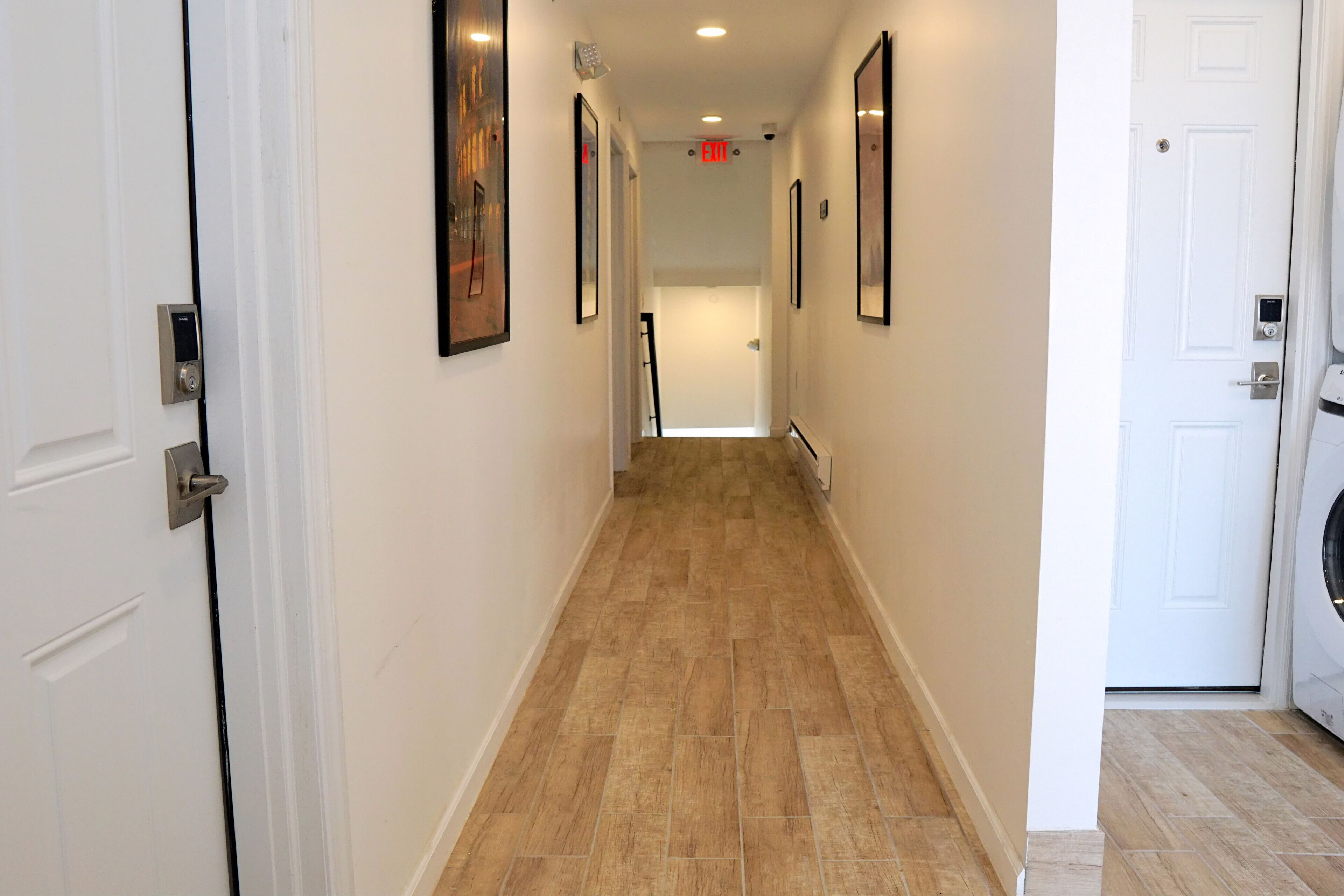 A hallway with white walls, a tiled floor, and framed pictures on the walls.