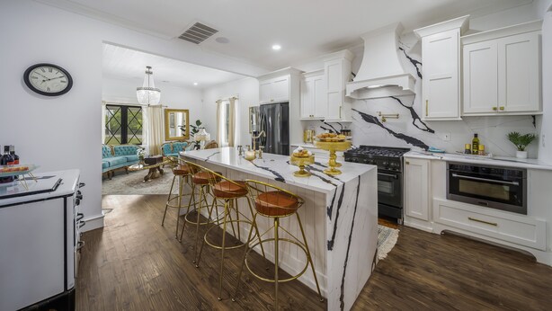 A modern kitchen with white cabinets, a marble island, and a bar area with stools.