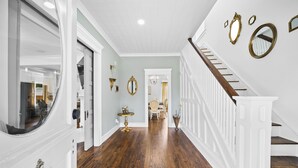A hallway with wooden flooring, white walls, and a staircase with white railings.