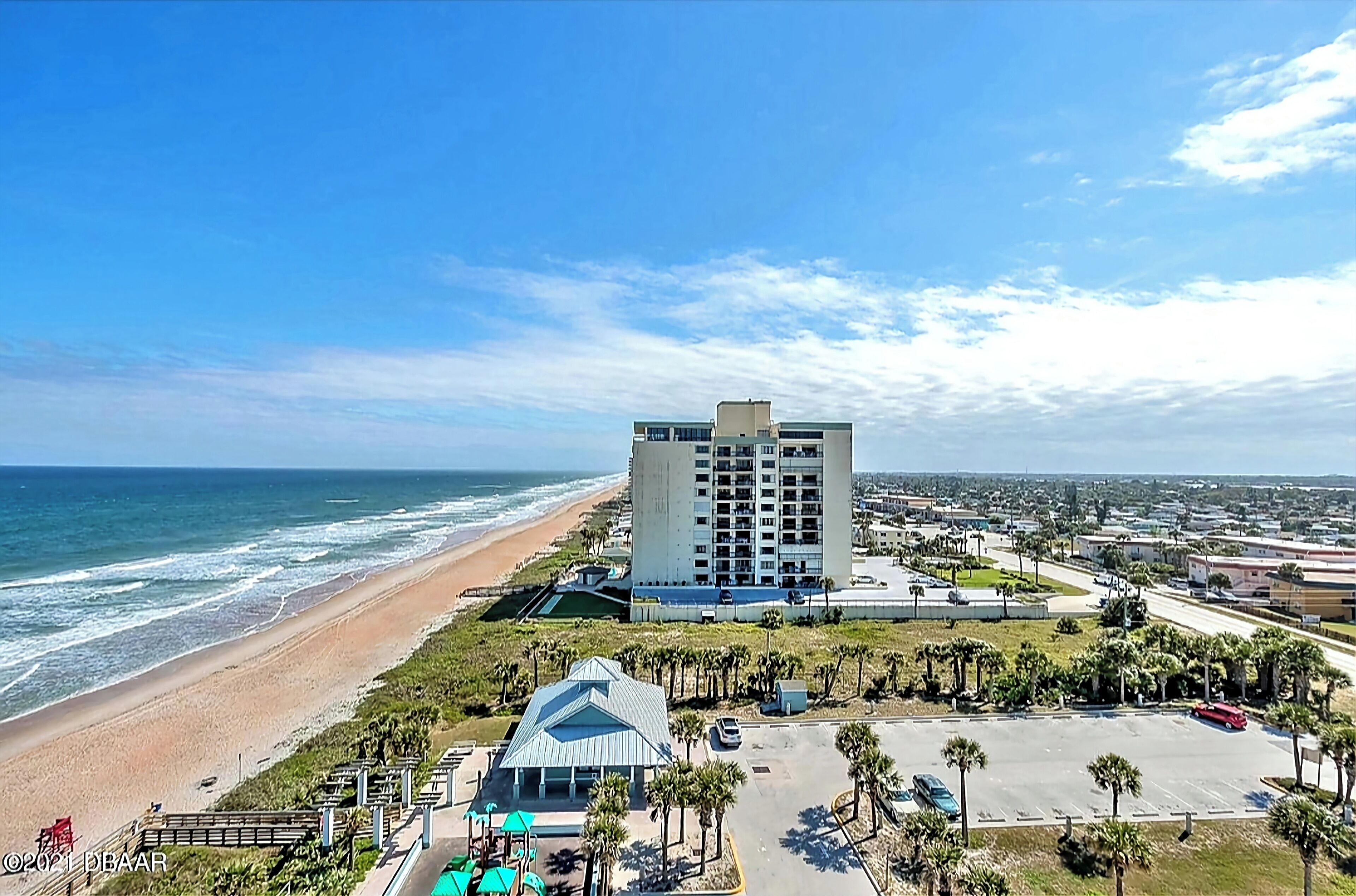 Un hotel costero con vista a la playa, estacionamiento y un edificio grande de varios pisos.