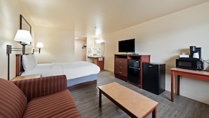 A hotel room with a bed, a sofa, a desk with a microwave, a refrigerator, and a television. - Quincy INN and Suites (Quincy)