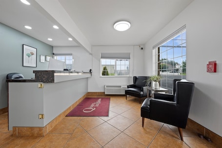 A reception area with a desk, chairs, a fire alarm, and a large window with a view.. Quincy INN and Suites