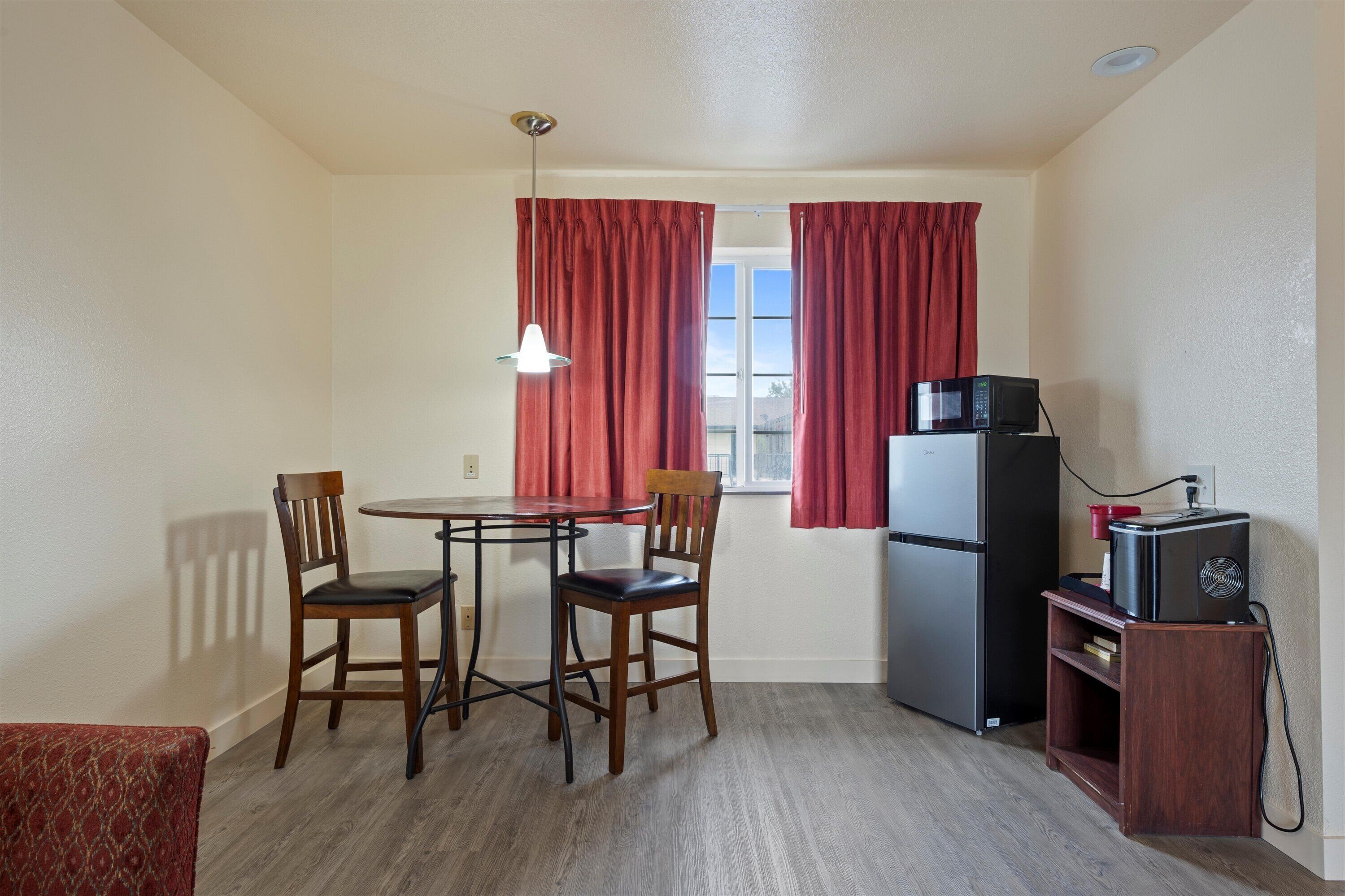 A compact kitchen with a dining table, two chairs, a refrigerator, a microwave, and a small wooden cabinet.