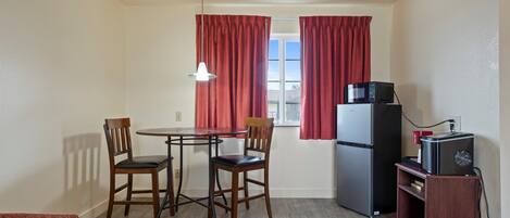 A compact kitchen with a dining table, two chairs, a refrigerator, a microwave, and a small wooden cabinet.