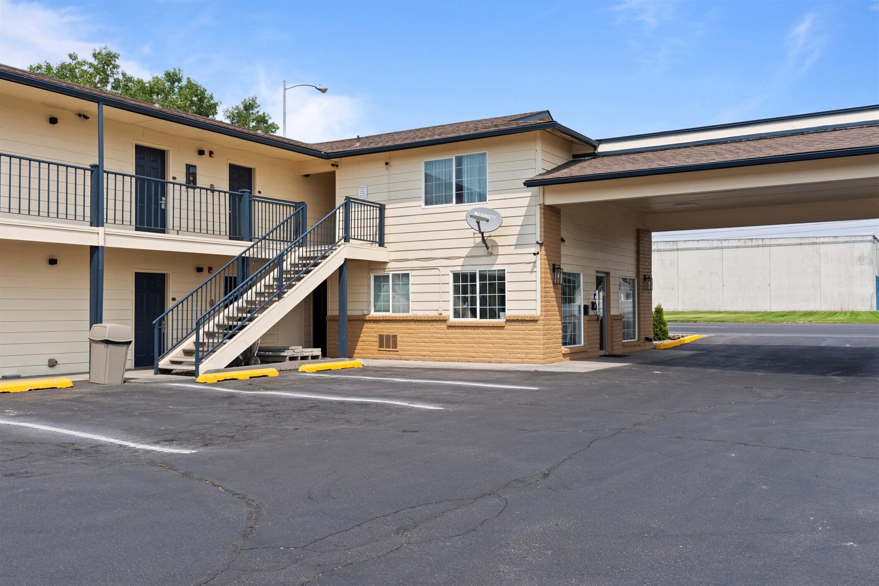 A two-story motel with a central staircase, a satellite dish, and a covered parking area.